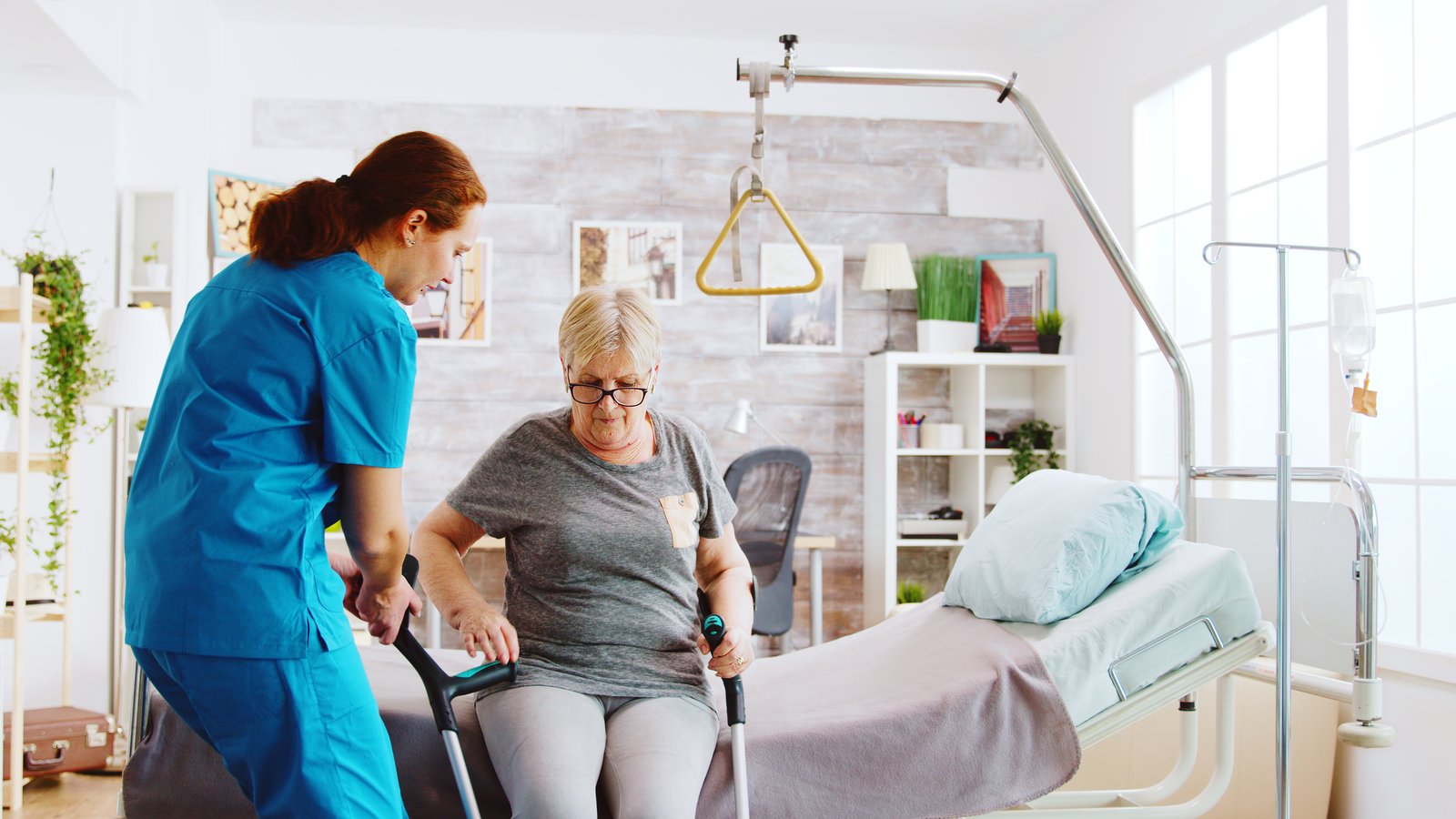 A nurse supporting an older woman walking with crutches